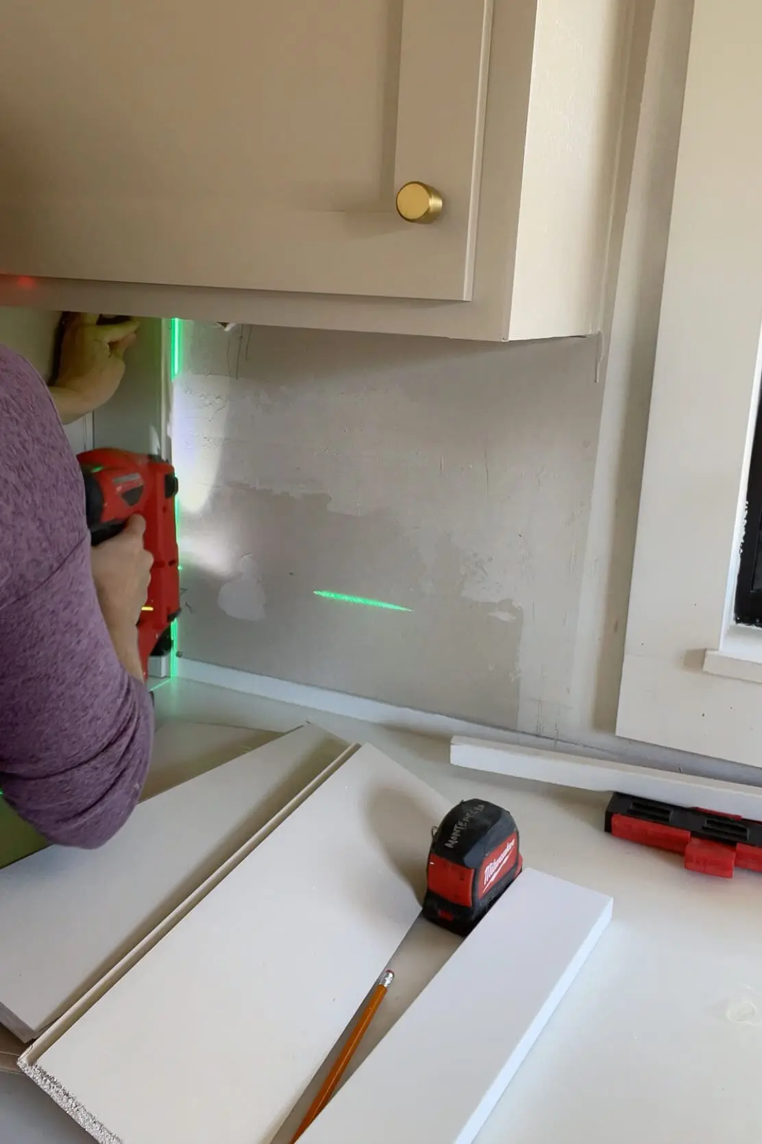 Using a laser level to keep a shiplap backsplash straight.